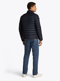 Navy puffer jacket with horizontal quilted pattern, high collar, and elastic cuffs. Paired with light blue pants and white sneakers.