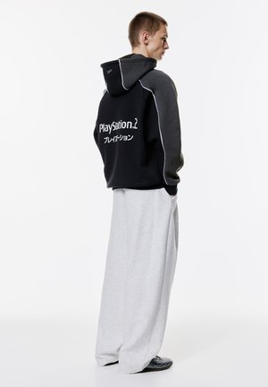 Black hoodie with white accents, featuring "PlayStation 2" logo. Paired with gray wide-leg pants and black shoes. Material appears soft.