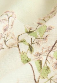 Látka s květinovým vzorem, která se vyznačuje jemným, texturovaným tkaním v krémové barvě s zelenými listy a jemnými růžovými květy, ukazuje přírodní design.