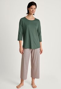 Top verde a maniche lunghe con scollatura rotonda abbinato a pantaloni larghi a pois chiari con design geometrico. Tessuto dalla texture liscia.