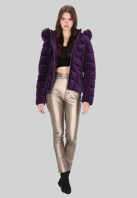 Fioletowa puchowa kurtka z zamkiem z przodu, elastycznymi mankietami i kapturem. Połączona z dopasowanymi, metalicznie złotymi spodniami i czarnymi skarpetkami.