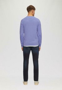 Malvefarbener Rundhalsausschnitt-Pullover, mit gestrickter Textur, kombiniert mit dunkelblauen Jeans. Der Pullover hat enganliegende Bündchen und Saum, schlichtes Design ohne Muster oder Akzente.