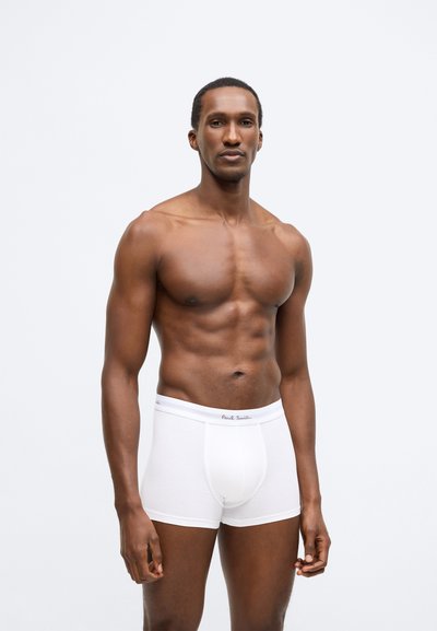 Weiße Boxershorts aus Baumwolle mit elastischem Bund und dezentem Branding vorne. Das Modell hat eine durchtrainierte Figur und steht vor einem schlichten Hintergrund.