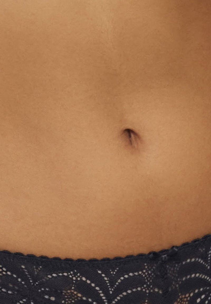 Schwarzer Spitzenbund mit floralem Muster, der einen glatten, braunen Bauch und einen nach innen stehenden Bauchnabel betont. Weiche Textur, intime Unterwäsche.