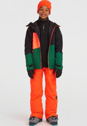 Svetlebarevný sněhový outfit se skládá z černé bundy s oranžovými a zelenými panely, jasně oranžových kalhot, černých rukavic a bot s modrými akcenty.