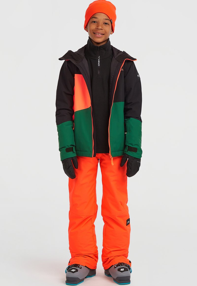 Ljust färgad snöklädsel bestående av en svart jacka med orange och gröna paneler, klara orangea byxor, svarta handskar och stövlar med blå accenter.