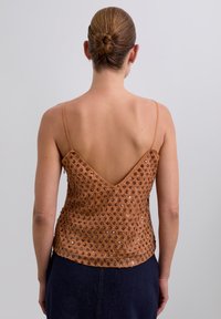 Top sin mangas marrón con un diseño de espalda en V, que presenta un tejido texturizado adornado con brillantes lentejuelas dispuestas en un patrón.