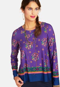 Lila Longsleeve-Oberteil mit floralen Kreisen und geometrischen Mustern, blauen Akzenten am Saum und bunten horizontalen Streifen.