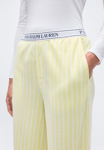 Άτομο που φοράει κίτρινο και λευκό ριγέ παντελόνι με λωρίδα μέσης "Polo Ralph Lauren", λευκό μακρυμάνικο πάνω μέρος, χέρι στην τσέπη.