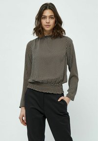 Top a maniche lunghe nero e beige con motivo, vita arricciata e scollatura a raccolto, abbinato a pantaloni neri.