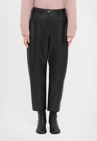 Zwarte faux leren broeken met hoge taille, recht model en zichtbare stiksels. Gecombineerd met zwarte enkellaarsjes.
