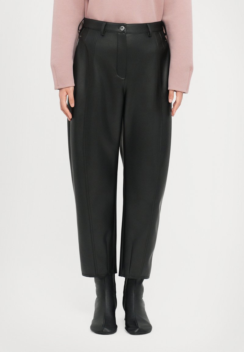 Zwarte faux leren broeken met hoge taille, recht model en zichtbare stiksels. Gecombineerd met zwarte enkellaarsjes.
