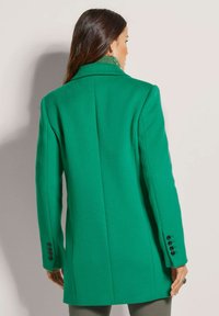 Groene wollen mixjas met een getailleerde pasvorm, notch-kraag, enkele split en knoopmanchetten, met een gladde, gestructureerde afwerking.