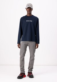 Marineblå langermet skjorte med teksten "RED BULL RACING", grå jeans og svarte/røde treningssko med kraftige såler. Lys grå cap med dekorasjoner.