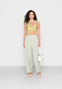 T-shirt transparente com padrão floral em rosa claro e verde; calças de cintura alta em verde claro; bolsa branca; sandálias de salto com detalhe floral.