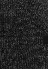 Cappellino nero lavorato a maglia con un motivo a trama, caratterizzato da un'applicazione liscia nera. Il materiale sembra morbido e spesso.