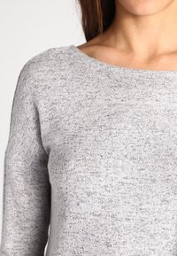 Szary dzianinowy sweter o miękkiej fakturze, szerokim dekolcie i subtelnym melanżowym wzorze. Posiada długie rękawy i luźny krój.