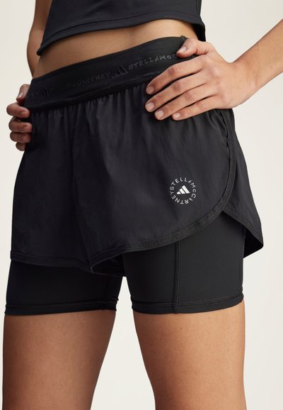 Sorte atletikshorts med et løst ydre lag og tætsiddende indre shorts. Har en struktureret elastik i taljen og en logodetalje på det ydre lag.