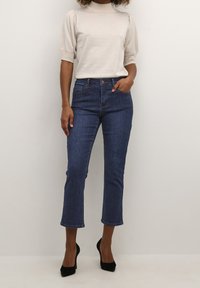 Ljusfärgad, texturerad topp med korta puffärmar, i kombination med högmidjade, korta mörkblå jeans och svarta högklackade skor.