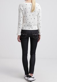 Suéter blanco de punto con lunares negros, de manga larga y puños acanalados, combinado con jeans negros de corte ajustado y zapatillas blancas.
