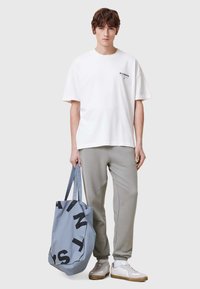 Vit oversized t-shirt med svart logotyp, grå sweatpants och en ljusblå tote bag med svart text, bärs med vita sneakers.