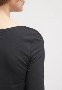 Haut noir ajusté avec une texture lisse et un col rond. L'arrière présente un design simple avec un léger détail de couture.