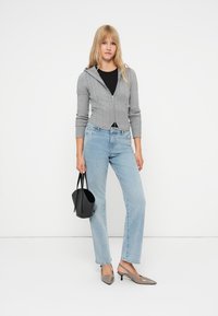 Pelēks īss kapuces jaku ar teksturētu rakstu, melna pieguļoša blūze, gaiši zili taisni džinsi, pelēki augstpapēžu apavi un melna rokassoma.