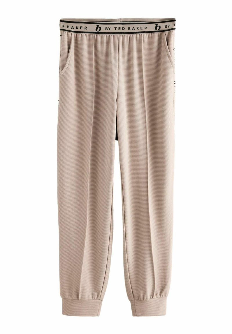 Beige joggerbukser med ribbet tekstur, elastisk talje med en sort label og sidelommer. Bunden er manchetteret for en tætsiddende pasform.
