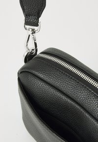 Black leather crossbody bag with a textured surface, silver zipper, and a detachable strap featuring a metallic clip.