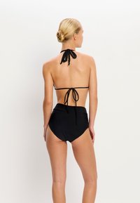 Ensemble de bikini noir avec un col halter et un bas taille haute. Comprend des bretelles à nouer et un tissu lisse et extensible.