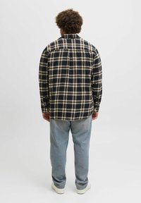 Sort og beige ternet flannel skjorte, lange ærmer, knaplukning ved håndleddene, afslappet pasform, parret med lyseblå jeans og hvide sneakers.