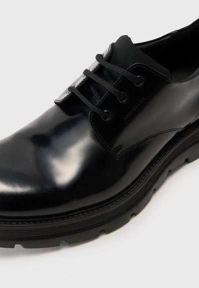 Black leather dress shoe with a glossy finish, featuring round laces, a padded collar, textured sole, and subtle branding on the side.