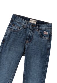 Jeans de mezclilla azules con un diseño clásico, cinco bolsillos y cierre de botón. Presenta un pequeño parche con el logo en el bolsillo delantero.