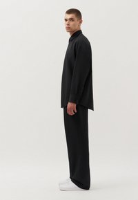 Zwarte lange mouwen shirt met een relaxte pasvorm en knoopmanchetten, gecombineerd met zwarte brede broek en witte sneakers. Gladde textuur.