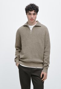 Pull-over côtelé marron clair avec un col demi-fermeture éclair, des manches longues, et une coupe décontractée ; porté sur une chemise blanche et assorti à un pantalon foncé.