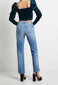 Blå jeans i denim med avslappnad passform, fem fickor och en lädermärke baktill. Bärs med en grön texturerad crop top och svarta klackar.