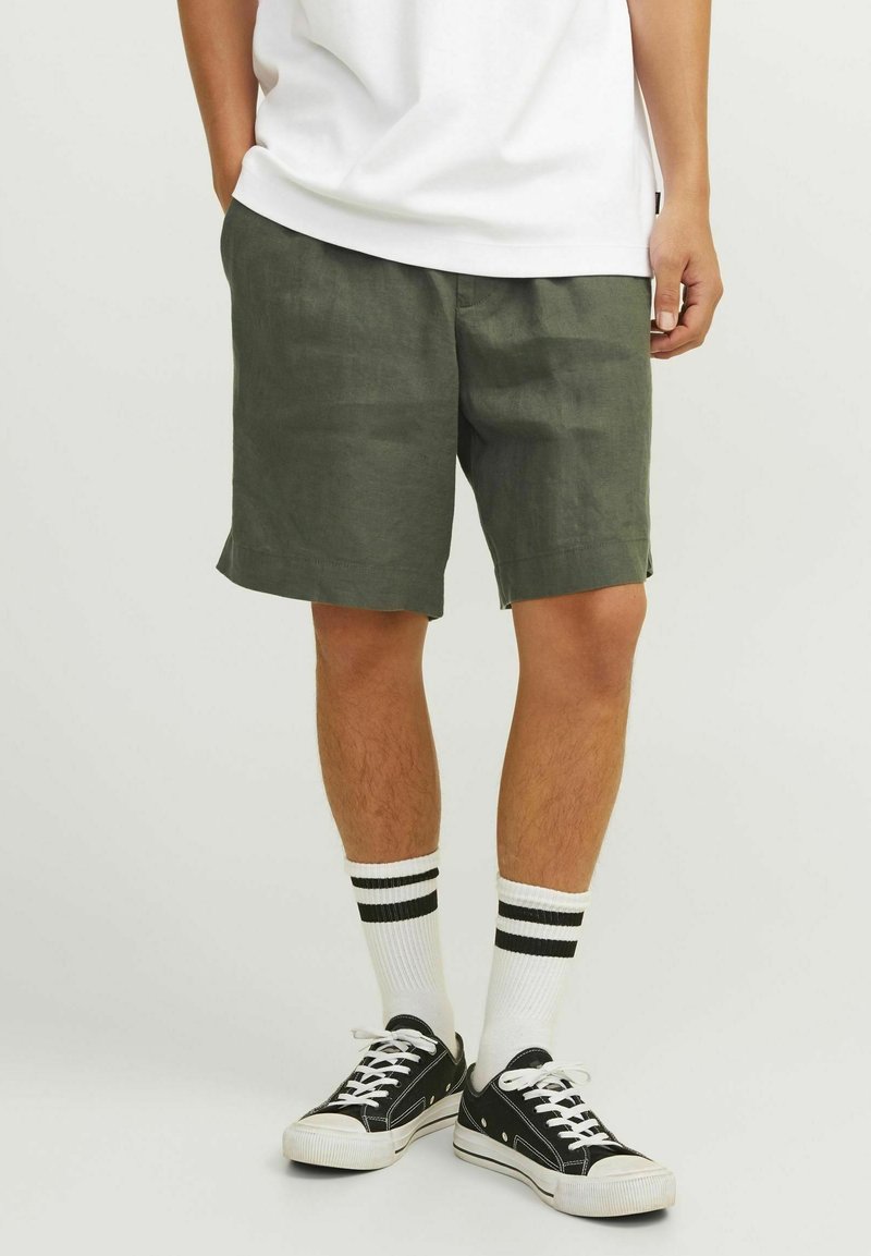 Olivgröna linnebyxor med avslappnad passform, sidofickor och en något sträv yta. Kombineras med svarta sneakers och randiga strumpor.