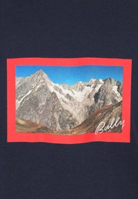 Granatowa koszulka z prostokątną grafiką pejzażu górskiego oprawioną na czerwono, z napisem "Bally" wydrukowanym białą kursywą.