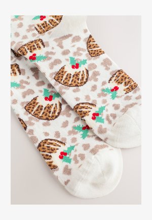 Baltos kojinės su leopardų kailio raštu, puoštos šventinių pudingo dizainų, akcentuotų žaliais lapeliais ir raudonomis uogomis. Be siūlių pėdos srityje.