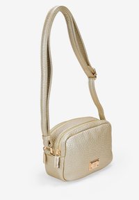 Bolso de mano texturizado dorado de forma rectangular, con compartimentos con cremallera y una larga correa para el hombro. Presenta un detalle de hardware en tono dorado.