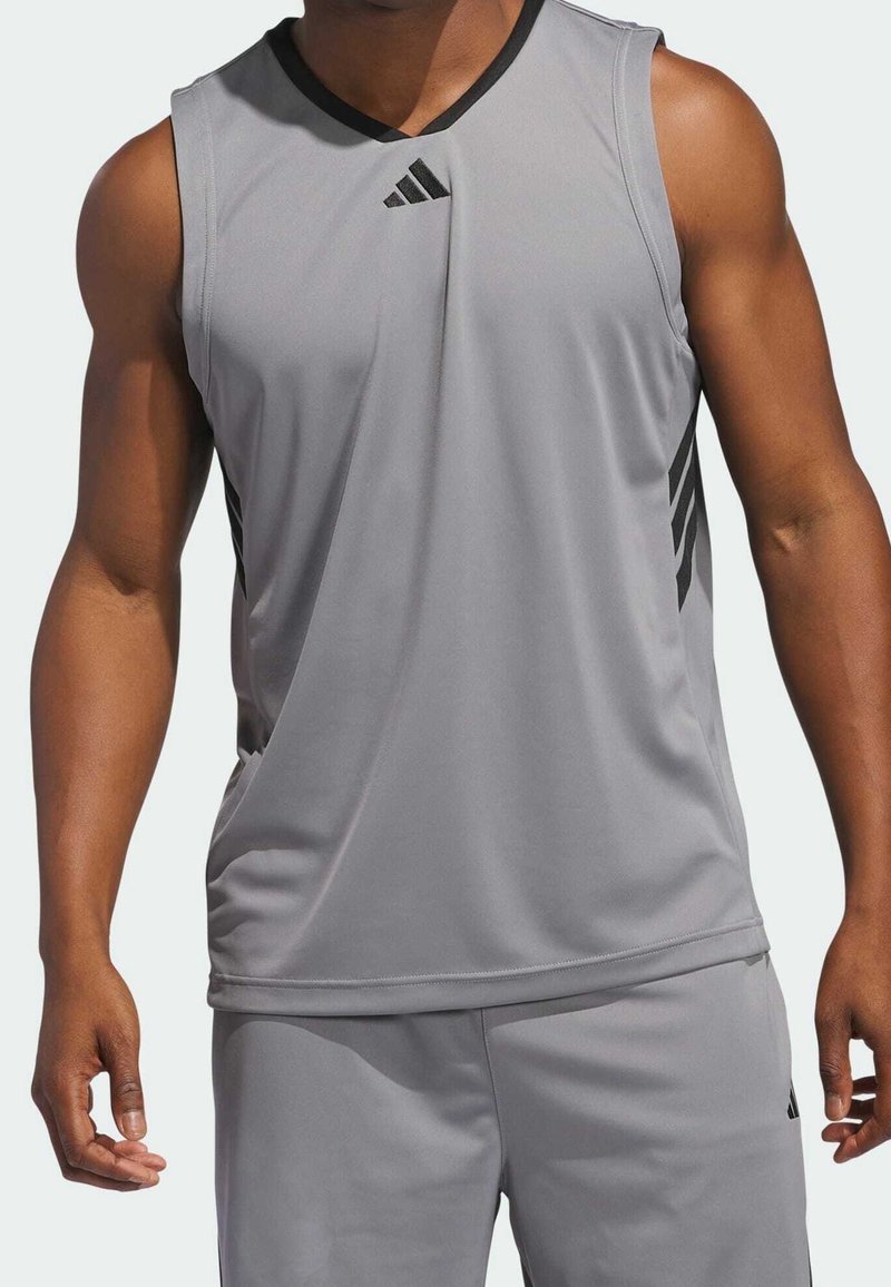 Personne athlétique portant un débardeur de sport gris et un short assorti avec un logo Adidas noir et des bandes.