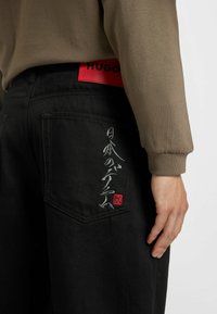 Schwarze Jeans aus Denim verfügen über ein rotes Logo-Patch am hinteren Bund und filigrane silberne Stickerei auf der hinteren Tasche.