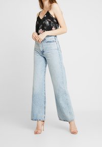 Hellblaue hoch taillierte Jeans mit weiten Beinen und fransigem Saum, kombiniert mit einem schwarzen, floralen Spaghetti-Top mit Spitze und dünnen Trägern.