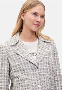 Gestructureerde tweed blazer in wit, beige en grijs. Heeft een notch-kraag, dubbelzijdige knopen en een getailleerde pasvorm.