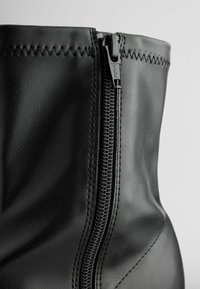 Black leather ankle boot with a vertical zipper, stitched detailing at the top, and a smooth, glossy texture.