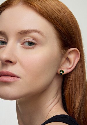 Złote kolczyki w kształcie liści z niebieskimi i zielonymi akcentami. Zbliżenie na ucho, ukazujące szczegółowy wzór i gładką teksturę na skórze.