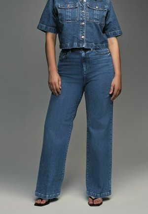 Geknipte spijkerjack met twee borstzakken en knoopsluiting, gecombineerd met hoge, wijde blauwe denim jeans. Glad van textuur.