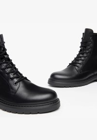 Schwarze Leder Stiefeletten verfügen über eine glatte Textur, eine runde Spitze und eine robuste Gummisohle. Sie sind mit Ösen und Schnürsenkeln für einen sicheren Sitz ausgestattet.