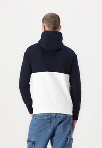 Navy and white color-blocked hoodie with a high neck and ribbed hem. Features a kangaroo pocket and is made of comfortable cotton fabric.