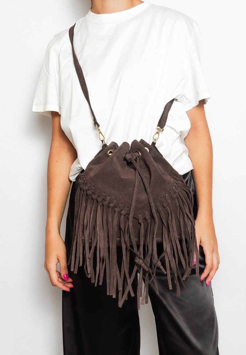Borsa in suede marrone con chiusura a coulisse e lunga frangia decorativa. Cinghia regolabile e rifiniture in metallo dorato.